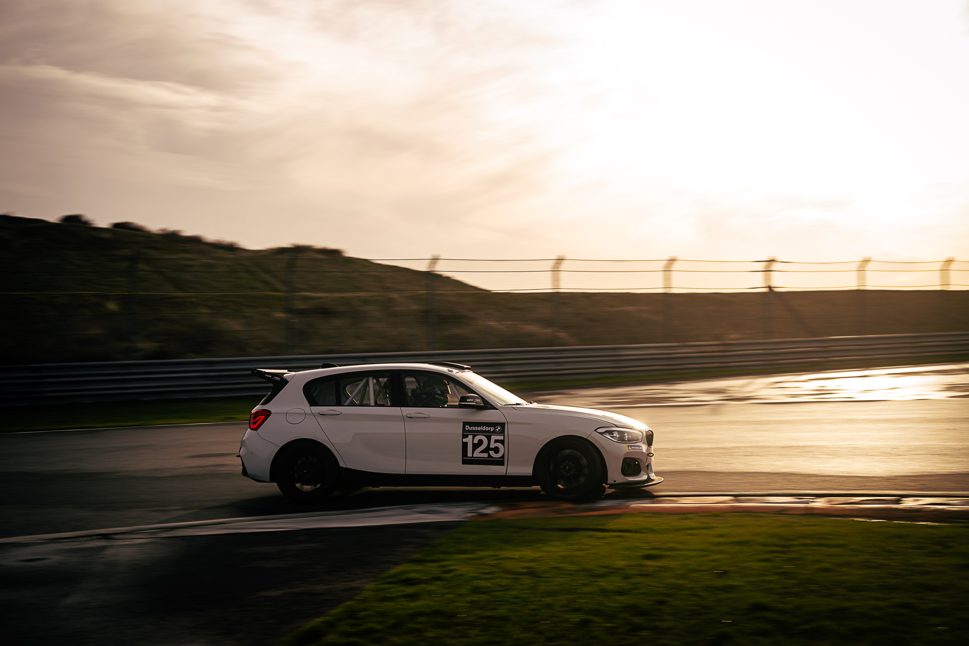 BMW M125i DayVtec BMW M125i DayVtec op Zandvoort tijdens zonsondergang op hoge snelheid.