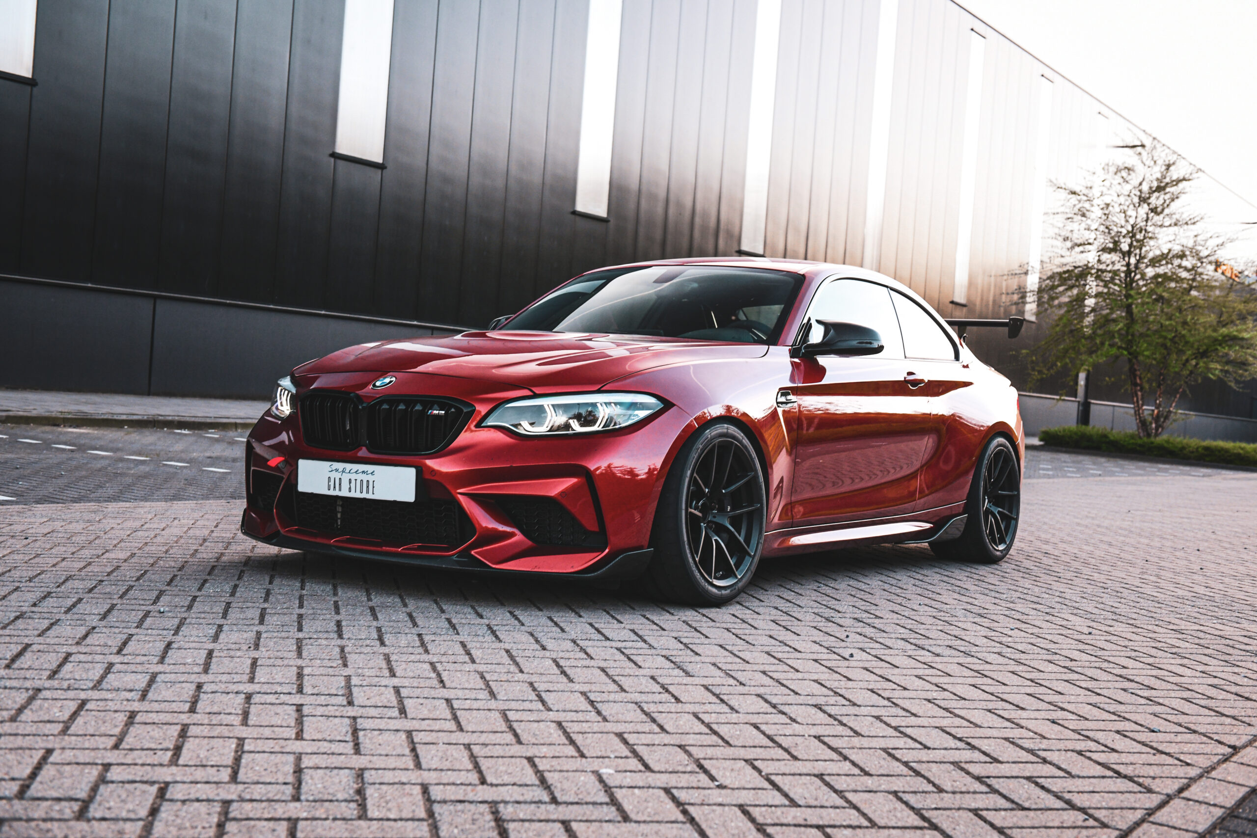 M2 Comp Oranje raceauto met zwarte wielen en spoiler. De auto is van het merk BMW en het model is een M2 Competition.