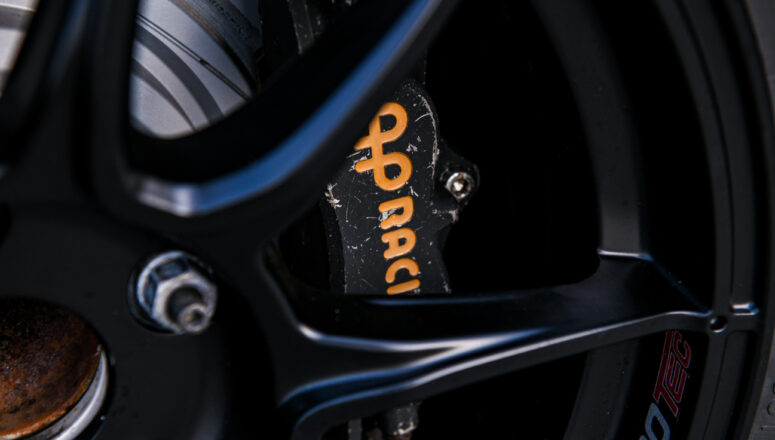 Zwarte remklauw met geel logo (Ap Racing) op de klauw. Deze is te zien langs de spaken van de zwarte wielen van de auto.